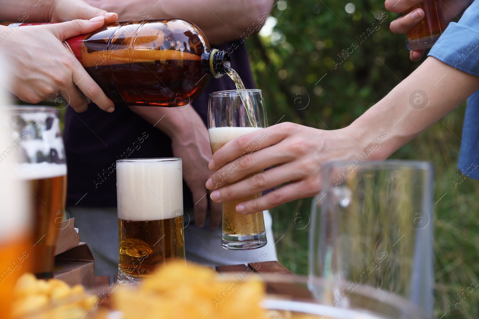 Photo of Young woman pouring beer into glass at table outdoors, closeup