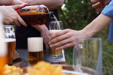 Photo of Young woman pouring beer into glass at table outdoors, closeup