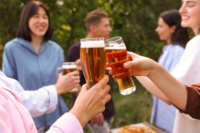 Photo of Group of happy friends clinking glasses of beer outdoors, selective focus