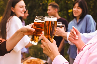 Photo of Group of happy friends clinking glasses of beer outdoors, selective focus