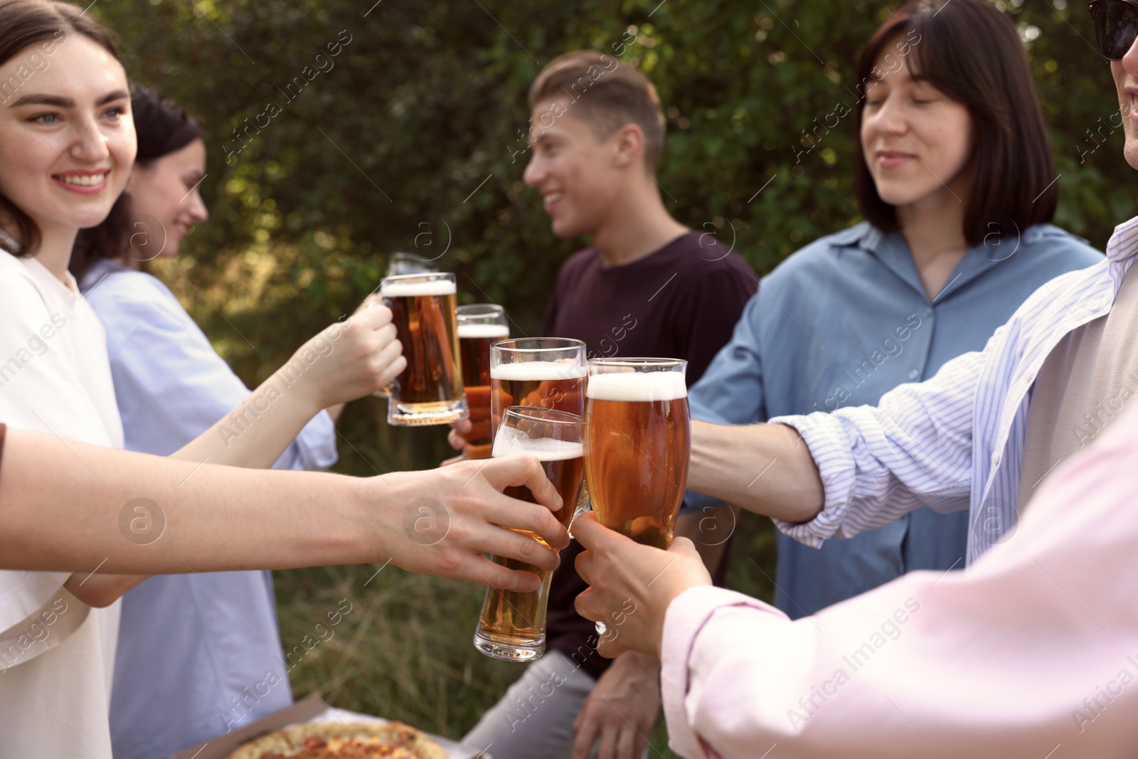 Photo of Group of happy friends clinking glasses of beer outdoors, selective focus