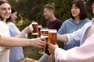 Photo of Group of happy friends clinking glasses of beer outdoors, selective focus