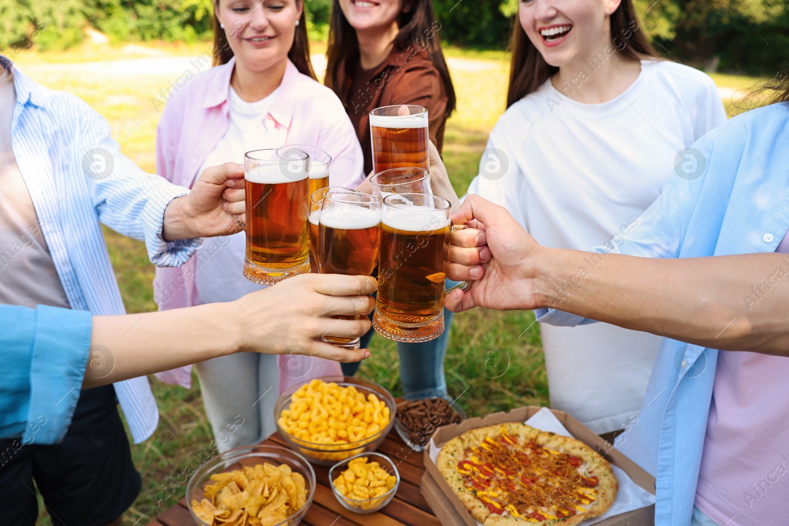 Photo of Group of happy friends clinking glasses of beer outdoors, selective focus
