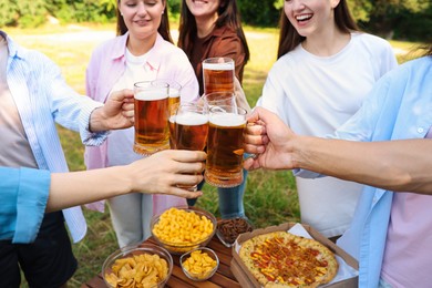Photo of Group of happy friends clinking glasses of beer outdoors, selective focus
