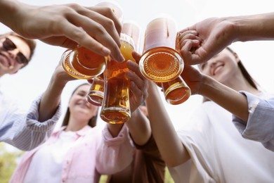 Photo of Group of happy friends clinking glasses of beer outdoors, bottom view