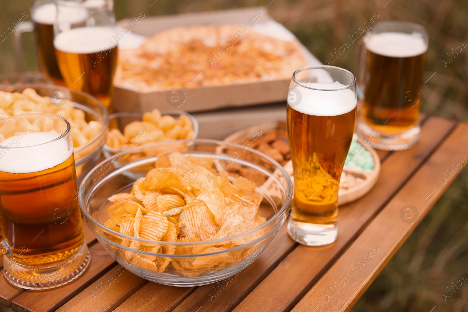 Photo of Glasses of beer and different snacks on wooden table outdoors, closeup