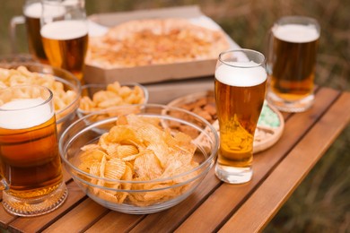 Photo of Glasses of beer and different snacks on wooden table outdoors, closeup