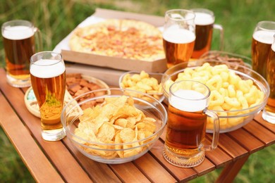 Photo of Glasses of beer and different snacks on wooden table outdoors, closeup