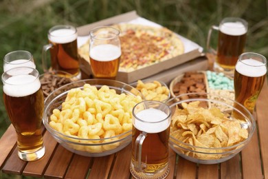 Photo of Glasses of beer and different snacks on wooden table outdoors, closeup