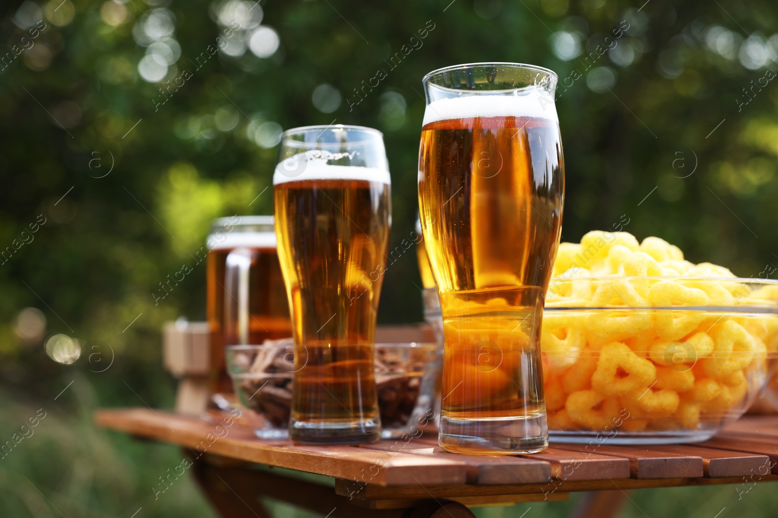 Glasses of beer and different snacks on wooden table outdoors, closeup Photo of Glasses of beer and different snacks on wooden table outdoors, closeup