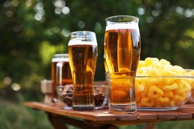 Photo of Glasses of beer and different snacks on wooden table outdoors, closeup