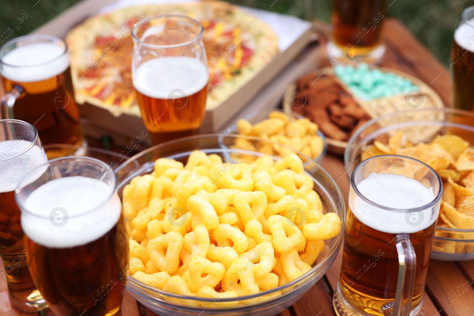 Photo of Glasses of beer and different snacks on wooden table outdoors, closeup