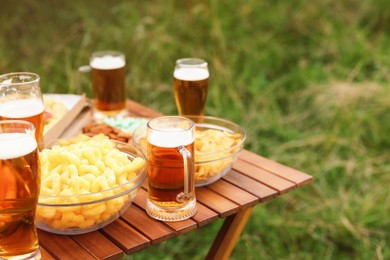 Photo of Glasses of beer and different snacks on wooden table outdoors, closeup. Space for text