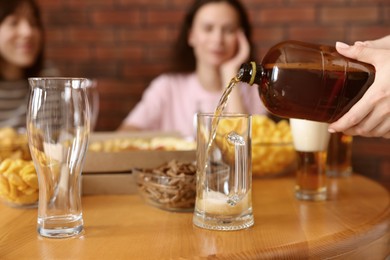 Photo of Woman pouring beer into glass at wooden table indoors, selective focus