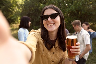 Photo of Young woman with beer taking selfie at party outdoors