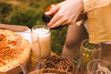 Photo of Young woman pouring beer into glass at table outdoors, closeup