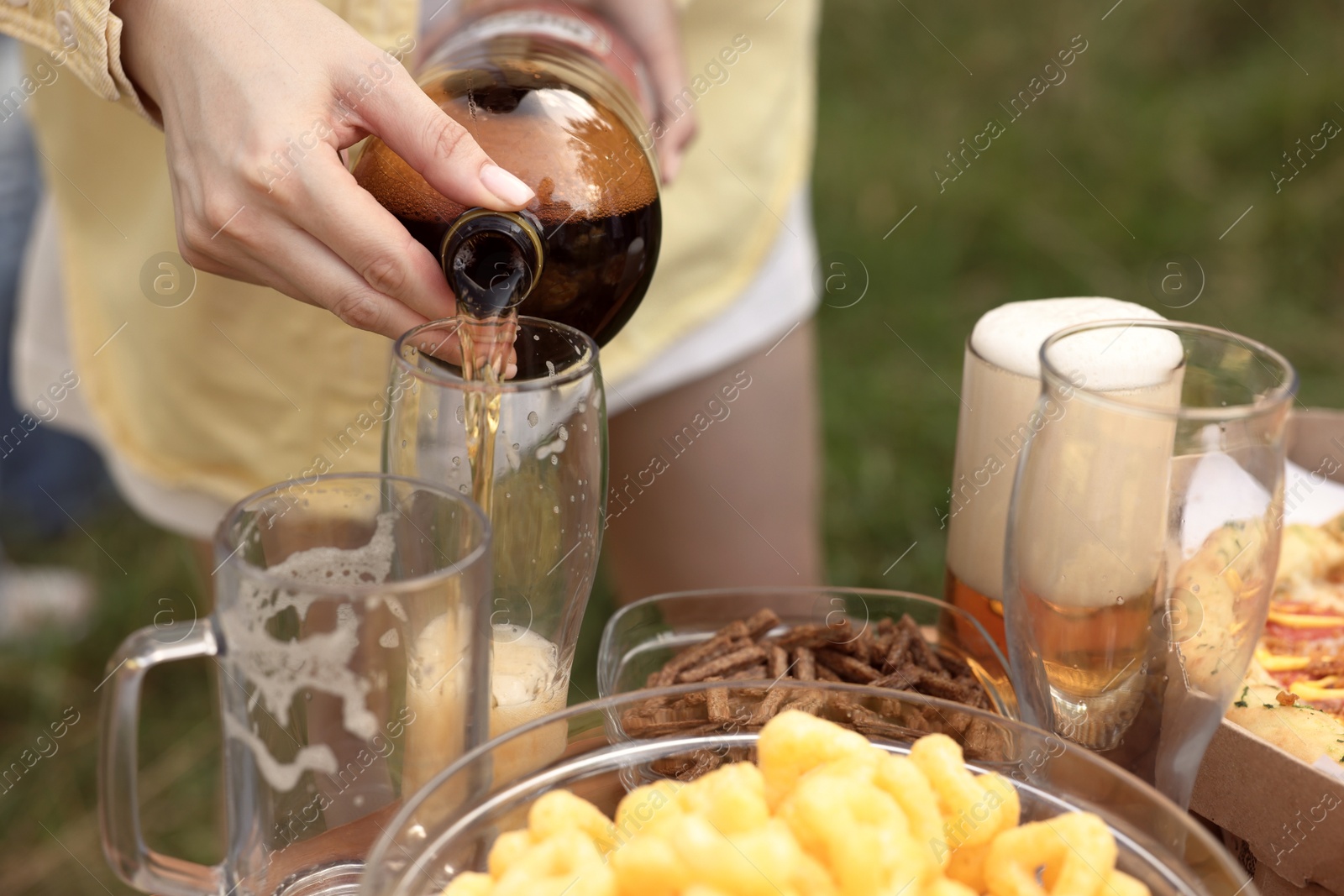 Photo of Young woman pouring beer into glass at table outdoors, closeup