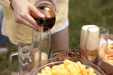 Photo of Young woman pouring beer into glass at table outdoors, closeup