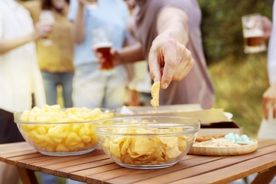 Photo of Group of happy friends with snacks having fun and drinking beer outdoors, selective focus