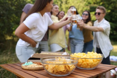 Photo of Group of happy friends having fun and drinking beer outdoors, focus on snacks