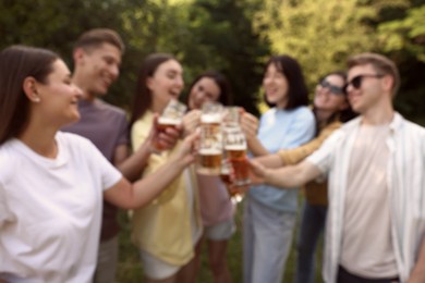 Photo of Blurred view of happy friends clinking glasses of beer outdoors