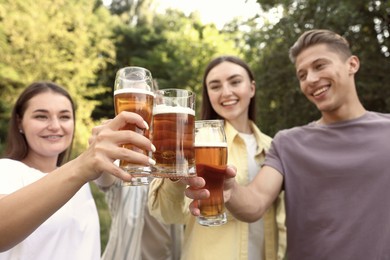 Photo of Group of happy friends clinking glasses of beer outdoors, selective focus