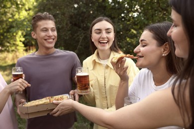 Photo of Group of happy friends with pizza having fun and drinking beer outdoors, selective focus