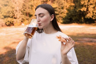 Photo of Young woman with tasty pizza drinking beer outdoors