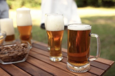 Photo of Glasses of beer and snacks on wooden table outdoors, closeup