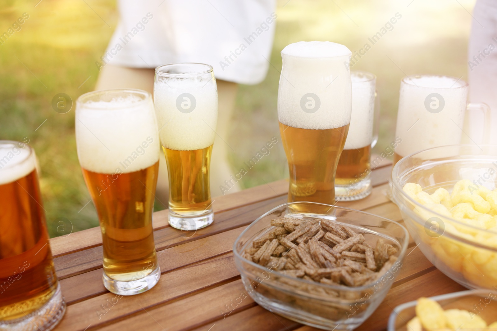 Glasses of beer and snacks on wooden table outdoors, closeup Photo of Glasses of beer and snacks on wooden table outdoors, closeup