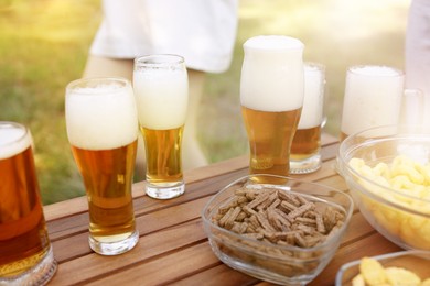 Photo of Glasses of beer and snacks on wooden table outdoors, closeup
