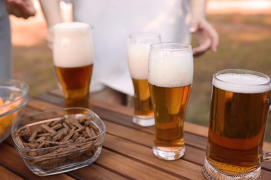Photo of Glasses of beer and snacks on wooden table outdoors, closeup