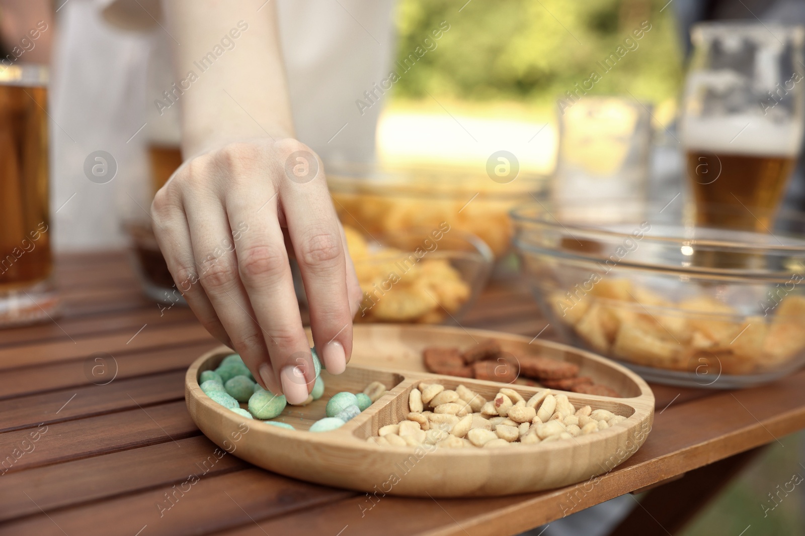 Woman with glass of beer taking snacks at wooden table, closeup Photo of Woman with glass of beer taking snacks at wooden table, closeup