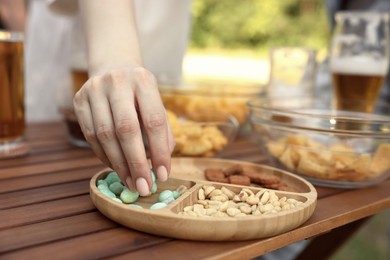 Photo of Woman with glass of beer taking snacks at wooden table, closeup