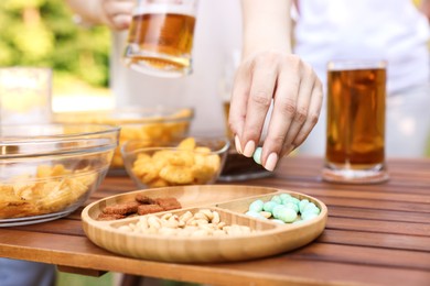 Photo of Woman with glass of beer taking snacks at wooden table, closeup