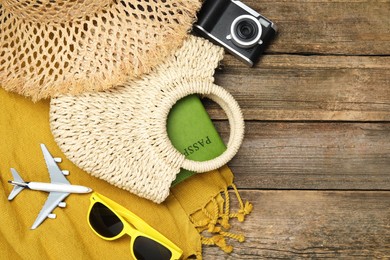 Photo of Time for summer vacation. Straw bag with passport, camera, toy plane, sunglasses and beach accessories on wooden background, flat lay. Space for text