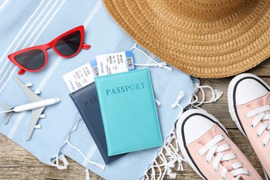 Photo of Passports, flight tickets, toy plane, shoes and beach accessories on wooden background, flat lay. Time for summer vacation