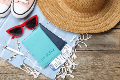 Photo of Passports, flight tickets, toy plane, shoes and beach accessories on wooden background, flat lay. Time for summer vacation