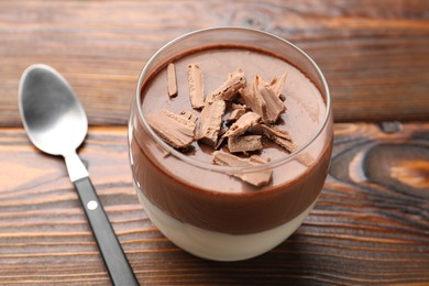 Photo of Delicious chocolate panna cotta in glass and spoon on wooden table, closeup