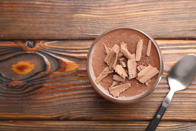 Photo of Delicious chocolate panna cotta in glass and spoon on wooden table, top view. Space for text