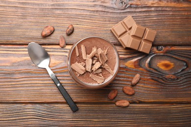 Photo of Delicious chocolate panna cotta in glass, cocoa beans and chocolate pieces on wooden table, flat lay