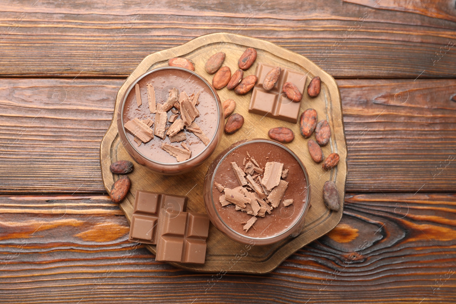 Photo of Delicious chocolate panna cotta in glasses, cocoa beans and chocolate pieces on wooden table, flat lay
