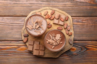 Photo of Delicious chocolate panna cotta in glasses, cocoa beans and chocolate pieces on wooden table, flat lay