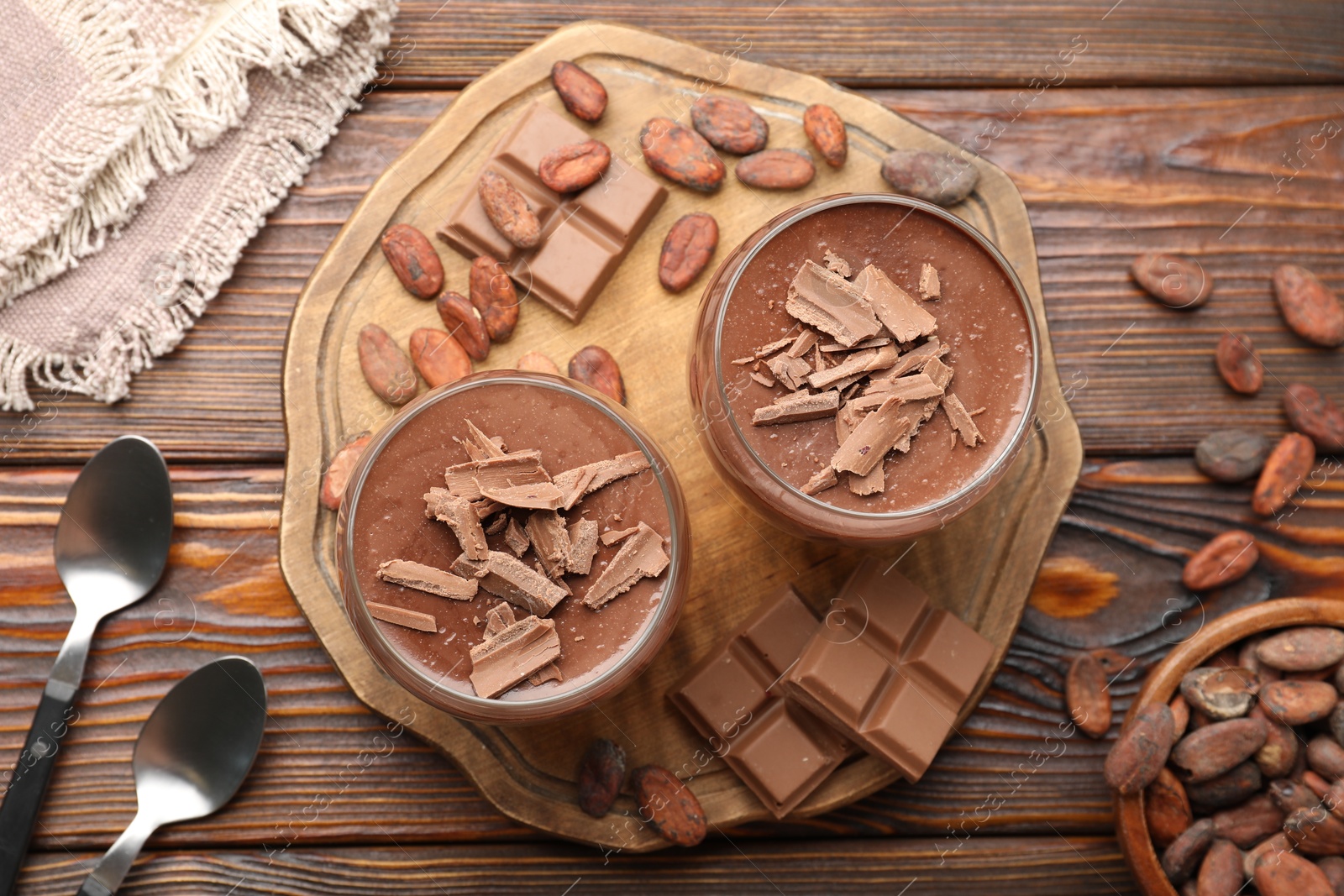 Photo of Delicious chocolate panna cotta in glasses, cocoa beans and chocolate pieces on wooden table, flat lay