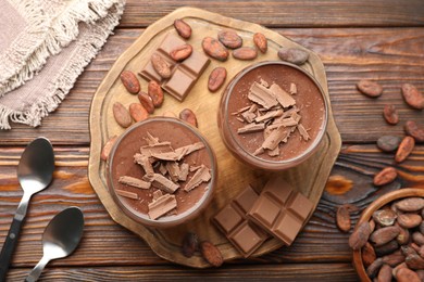 Photo of Delicious chocolate panna cotta in glasses, cocoa beans and chocolate pieces on wooden table, flat lay