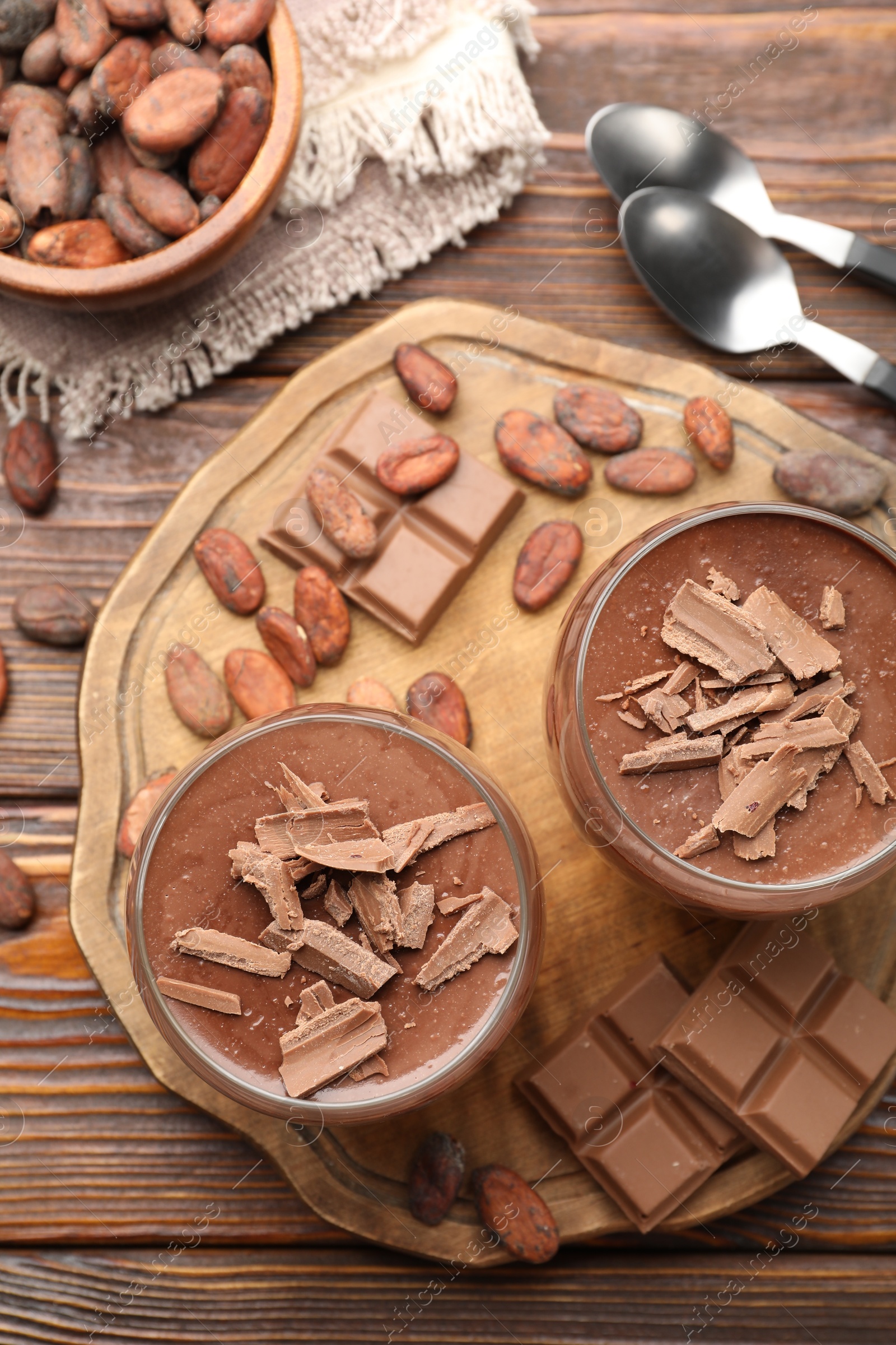Delicious chocolate panna cotta in glasses, cocoa beans and chocolate pieces on wooden table, flat lay Photo of Delicious chocolate panna cotta in glasses, cocoa beans and chocolate pieces on wooden table, flat lay