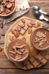 Photo of Delicious chocolate panna cotta in glasses, cocoa beans and chocolate pieces on wooden table, flat lay