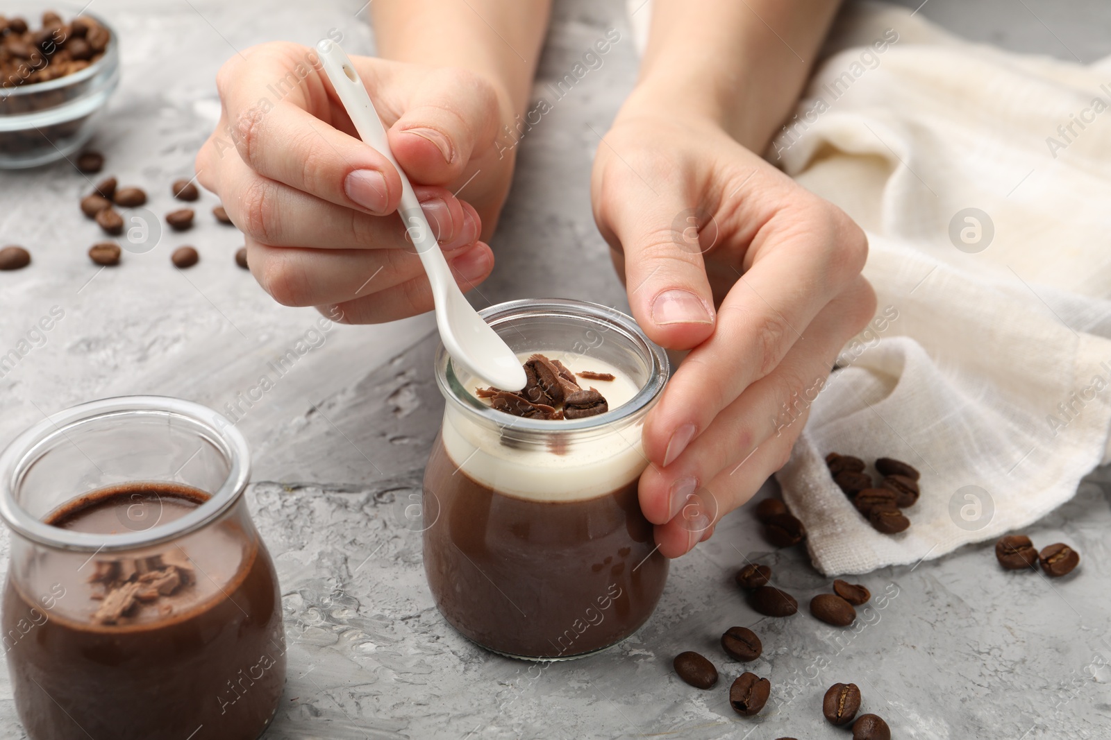 Photo of Woman eating delicious panna cotta with chocolate chunks and coffee beans at grey textured table, closeup