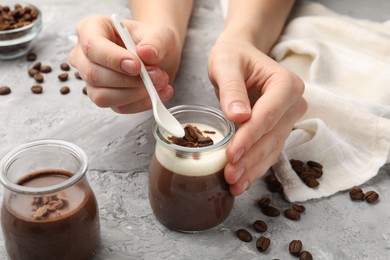 Photo of Woman eating delicious panna cotta with chocolate chunks and coffee beans at grey textured table, closeup
