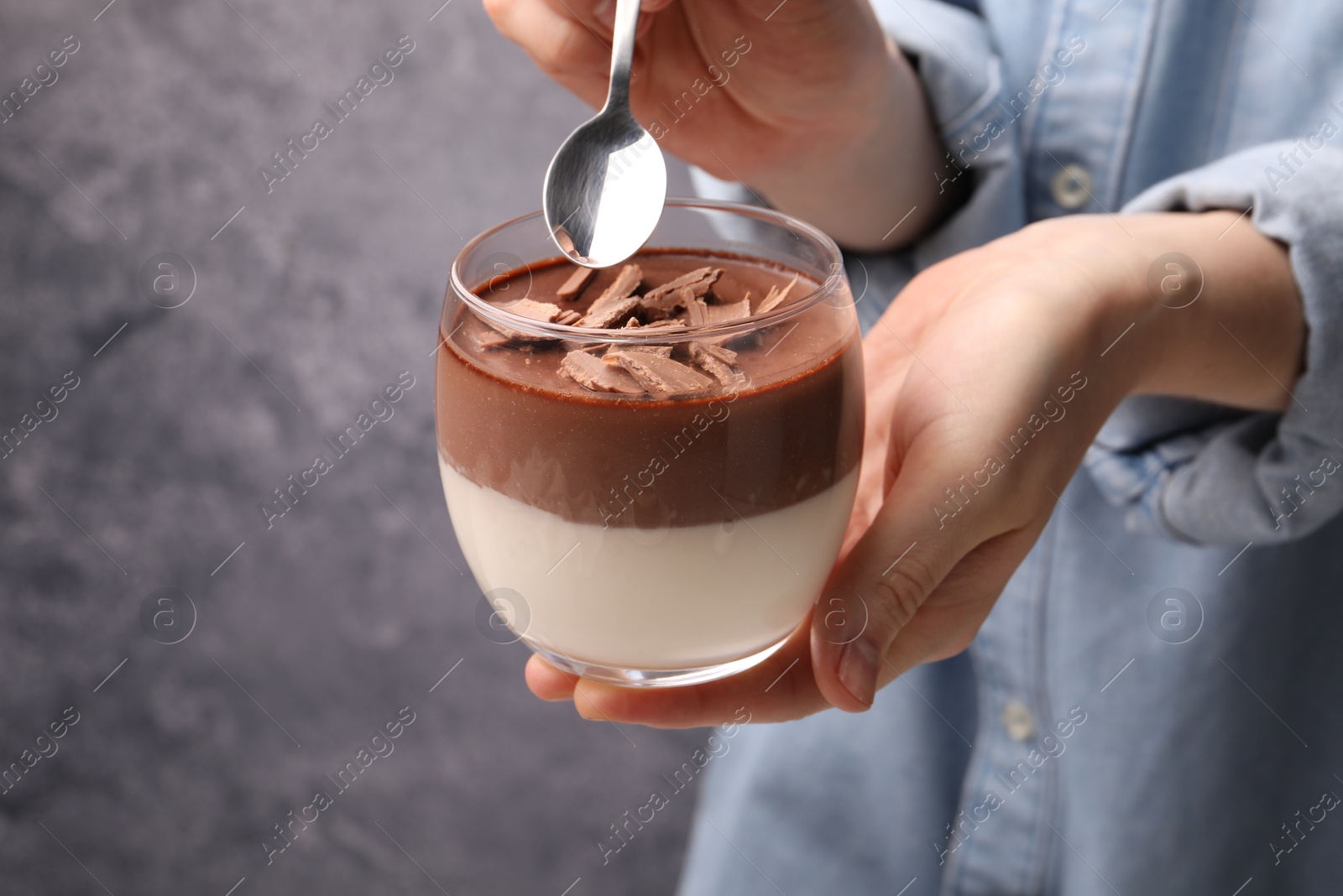 Photo of Woman holding glass with delicious panna cotta against grey background, closeup